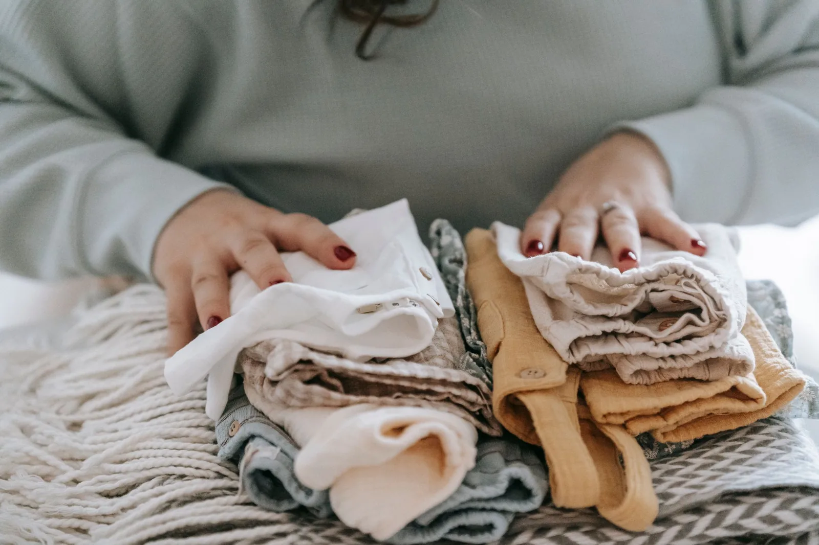 Two hands resting on stacks of clean, folded baby clothes
